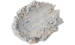 A medium circular puddle of some creamy ivory cleanser that has some pieces of crushed up Blueberries running through it, on a white background.