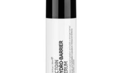 A tall cylindrical bright white plastic Bottle with a black plastic lid that has The INKEY List ectoin Hydro Barrier Serum written in bold black writing and a picture of a black stripe on it, on a white background.