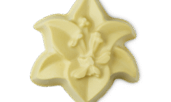 A small creamy pale cream six petalled lily shaped block of soap that has some lily petals and a stamen engraved on it, on a white background.