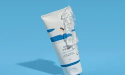 A tall conical bright white plastic Tube with a bright white plastic Lid that has Round Lab Birch Juice Moisturising Cleanser written in bold black writing, a picture of a bright blue stripe, a picture of a bright blue wave, and a picture of a person on it, on a bright blue background.