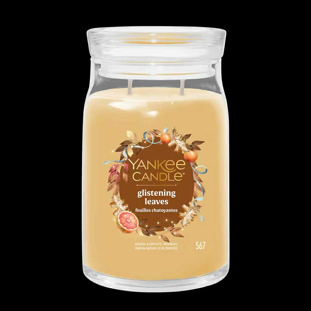 Fall Is Such A Fantastic Time Of The Year | Yankee Candle Fantastical Fall Collection A tall cylindrical glass jar full of some pale brown wax with a label that has Yankee Candle written in bright white writing, glistening Leaves written in bright white writing, and a picture of some golden orange leaves, some oranges, a slice of Fig, and a gold ribbon on it, on a black background.