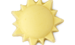 A medium bright yellow sun shaped block of solid massage oil that has some pointed Sunrayes engraved all over it, on a white background.