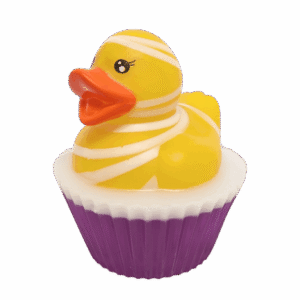 A large circular bright white cupcake shaped block of soap that has a dark purple paper cupcake case around it and a bright Yellow Rubber Duck with a bright orange beak that’s covered in some bright white bandages on top of it, on a white background.
