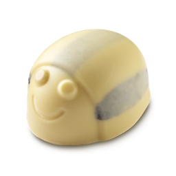 A shiny pale golden yellow bummble bee shaped block of solid Body Scrub that has some black stripes all over it and a large smiling face engraved on it, on a light grey background.