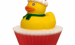A large circular bright white cupcake shaped block of soap that has a bright red paper cupcake case around it and a bright Yellow Rubber Duck with a bright orange beak, a bright red Santa’s Hat, and a dark green scarf sat on top of it, on a white background.