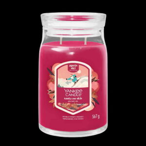A tall cylindrical glass Jar full of some bright pink Wax with a Label that has Yankee Candle written in bright white writing, Santa On Skis written in bright white writing, and a picture of Santa skiing on some snowy bright white mountains surrounded by some dark green pine trees on it, on a white background.