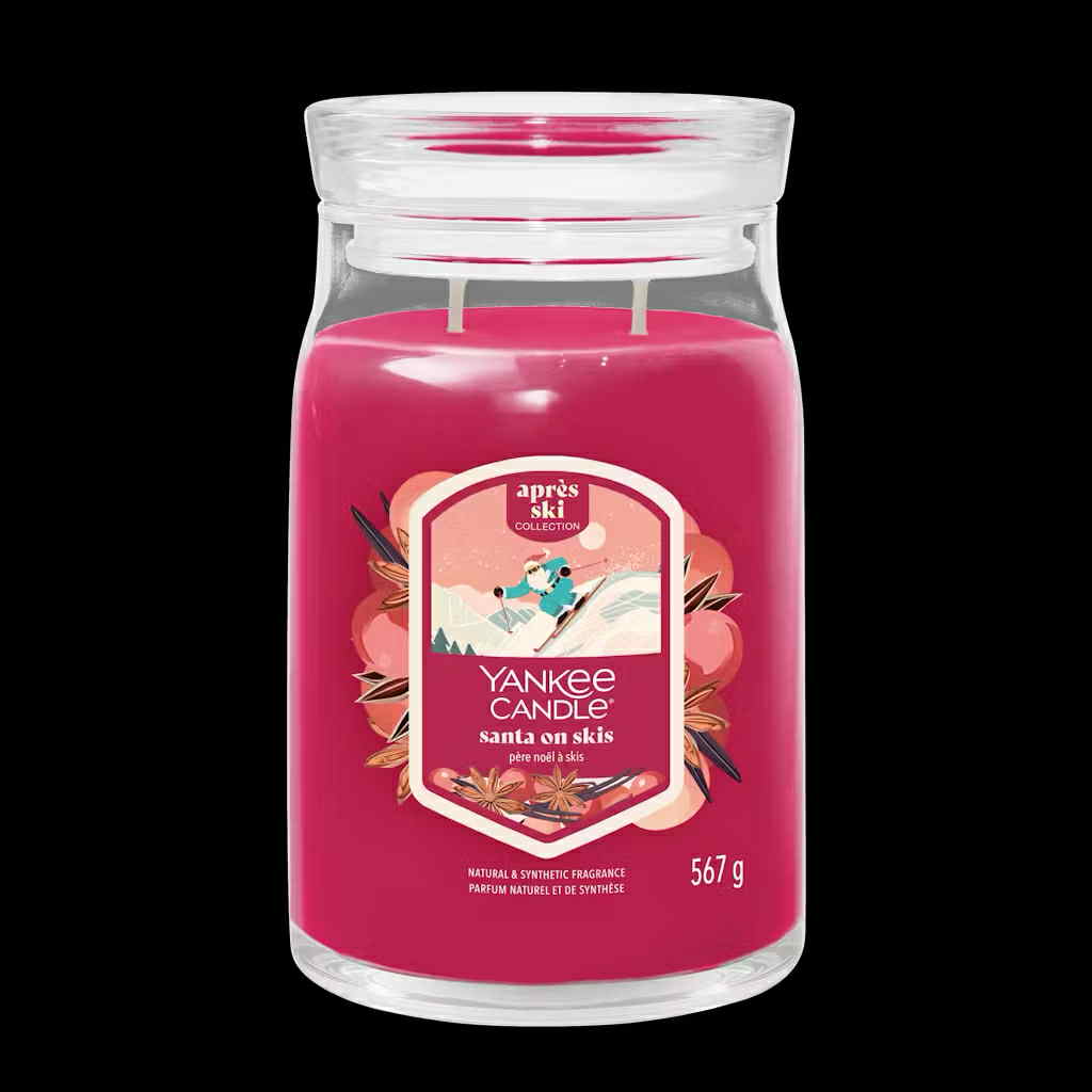Flying Down The Slopes This Christmas | Yankee Candle Après Ski Collection A tall cylindrical glass Jar full of some bright pink Wax with a Label that has Yankee Candle written in bright white writing, Santa On Skis written in bright white writing, and a picture of Santa skiing on some snowy bright white mountains surrounded by some dark green pine trees on it, on a white background.