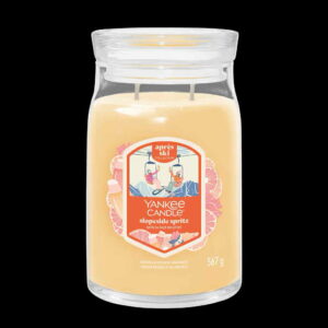 A tall cylindrical glass Jar full of some light Peach Wax with a Label that has Yankee Candle written in bright white writing, Slopeside Spritz written in bright white writing, and a picture of two smiling people drinking a glass of some fizzy clear liquid sat on a ski lift on it, on a white background.