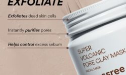 A short cylindrical bright white Plastic Tub with a bright white Plastic Lid that has INNISFREE Super Volcanic Pore Clay Mask written in dark brown writing on it surrounded by some small smudges of dark grey volcanic clay and a medium piece of dark grey rock, on a light beige background.