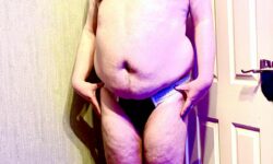 A tall bearded man with his hands on his hips wearing a pair of black briefs that has some white trim all over the seems and a white waistband that has M:R Underwear written in bold black writing on it stood against a white wooden door.