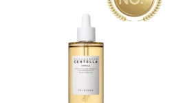 A tall cylindrical clear glass bottle full of some golden yellow liquid with a bright white Rubber Pipette lid and a bright white label that has Skin1004 Madagascar Centella Ampoule written in bold black writing on it, on a white background.