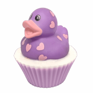 A large circular bright white cupcake shaped block of soap that has a pale Lilac paper cupcake case around it and a bright purple Rubber Duck with a bright orange beak, some large eyes, and some bright pink heart shapes all over it sat on top of it, on a white background.