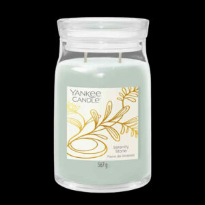 A tall cylindrical glass Jar full of some pale mint green Wax with a bright white label that has Yankee Candle written in bold black writing, Serenity Stone written in bold black writing, and a picture of a stylised gold plant on it, on a black background.