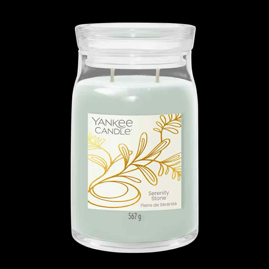 What I Thought of the Yankee Candle Advent House 2014 A tall cylindrical glass Jar full of some pale mint green Wax with a bright white label that has Yankee Candle written in bold black writing, Serenity Stone written in bold black writing, and a picture of a stylised gold plant on it, on a black background.