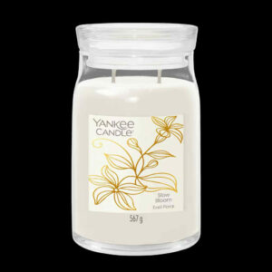 A tall cylindrical glass Jar full of some creamy white Wax with a bright white label that has Yankee Candle written in bold black writing, Slow Bloom written in bold black writing, and a picture of two stylised gold flowers with five long open petals on it, on a black background.