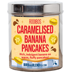 A tall cylindrical bright silver metal tin with a bright silver lid and a pale yellow label that has Caramelised Banana Pancakes loose Leaf Tea written in bright red writing and some pictures of some slices of bright yellow bananas and some dark brown puddles of Caramel Sauce on it, on a white background.