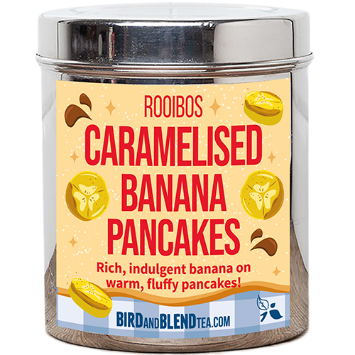 A tall cylindrical bright silver metal tin with a bright silver lid and a pale yellow label that has Caramelised Banana Pancakes loose Leaf Tea written in bright red writing and some pictures of some slices of bright yellow bananas and some dark brown puddles of Caramel Sauce on it, on a white background.