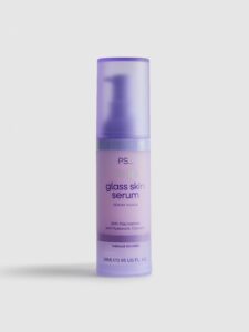 A short cylindrical bright Purple Bottle with a bright purple pump lid that’s covered by a matte semi-translucent purple plastic cap lid that has Primark PS… Glass Skin Face Serum written in dark purple writing on it, on a white background.