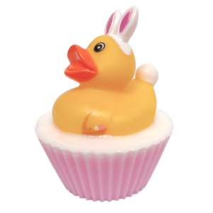 A large circular bright white cupcake shaped block of soap that has a light pink paper cupcake case around it and a bright yellow Rubber Duck with a bright orange beak, a large black eye, some bright white bunny ears, and a bright white puffy Tail sat on top of it, on a white background.