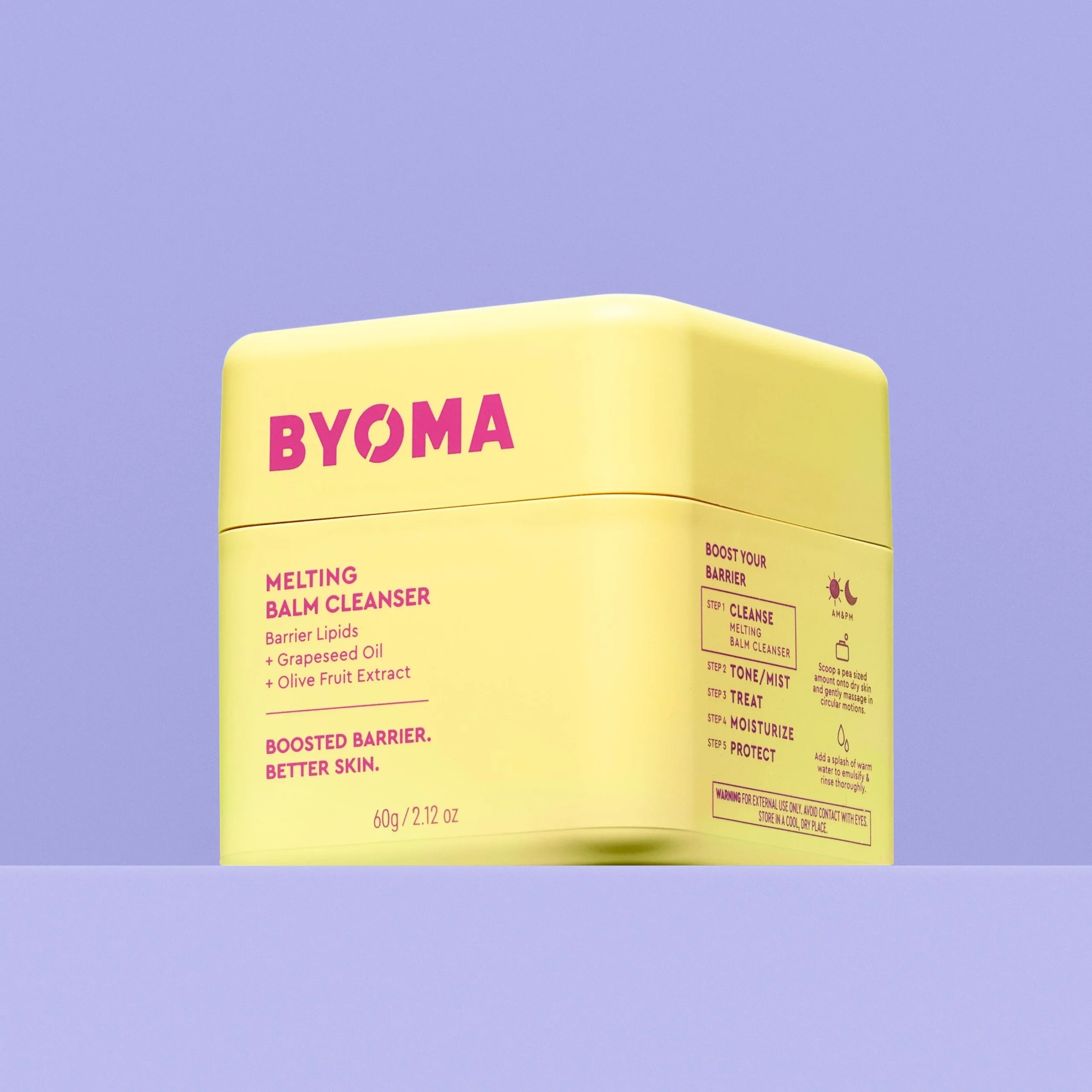 By Heck, that's some Cleansed & Nourished Skin | Byoma Melting Balm Cleanser A short rounded cube shaped bright yellow plastic tub that has Byoma Melting Balm Cleanser written in bright pink writing on it, on a light purple background.