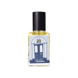 A short rectangular glass perfume bottle full of some translucent yellow liquid with a metallic black lid and a white label that has a picture of a blue illustration of a bright blue stone doorway that has 29 written in dark blue writing inside a circle above it and High street written in dark blue writing below it on it, on a white background.