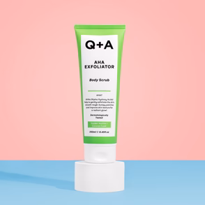Answering The Age-Old Question Of Why Don't I Have A Smooth Body? | Q+A AHA Exfoliator Body Scrub A tall cylindrical gradient bright green and white plastic Tube with a white plastic lid and a bright white label that has Q+A AHA Exfoliator Body Scrub written in bold black writing on it on a bright blue worktop, on a gradient bright pink background.