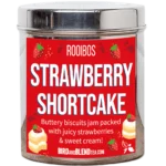 Tea Tastes Terrific | Bird & Blend Tea Company Tea & Biscuits Collection A tall cylindrical bright silver metal tin with a bright silver metal lid and a bright red label that has Strawberry Shortcake loose Leaf Tea written in bright white writing and some pictures of some golden brown cream-topped shortcake biscuits, some bright red strawberries, and some bright red swirls on it, on a white background.