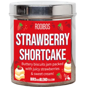 A tall cylindrical bright silver metal tin with a bright silver metal lid and a bright red label that has Strawberry Shortcake loose Leaf Tea written in bright white writing and some pictures of some golden brown cream-topped shortcake biscuits, some bright red strawberries, and some bright red swirls on it, on a white background.