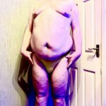 A tall bearded man with his hands on his hips wearing a pair of pale lemon yellow briefs with a pale lemon yellow Waistband that has Box Menswear written in bold black writing on it stood against a white wooden door.