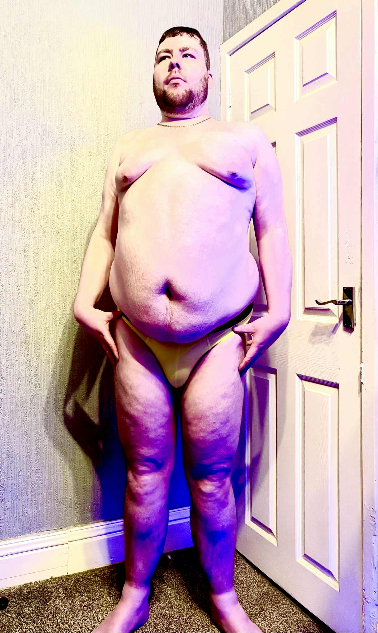 A tall bearded man with his hands on his hips wearing a pair of pale lemon yellow briefs with a pale lemon yellow Waistband that has Box Menswear written in bold black writing on it stood against a white wooden door.