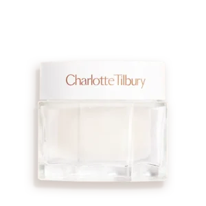 A short rounded square clear glass jar full of some thick creamy white liquid with a metallic white lid and a white label that has Charlotte Tilbury Charlotte’s Magic Water Cream written in bright Rose Gold writing on it, on a white background.
