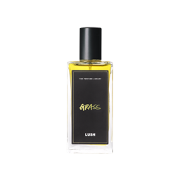 A tall rectangular clear glass bottle full of some amber coloured liquid with a metallic black lid and a black label that has Lush Perfume Library written in bright white writing and Grass written in bright yellow writing on it, on a white background.