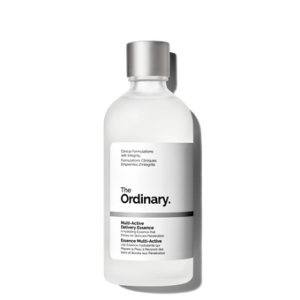 A tall cylindrical frosted glass bottle with a metallic silver lid and a bright white label that has The Ordinary Multi-Active Delivery Essence written in bold black writing on it, on a white background.
