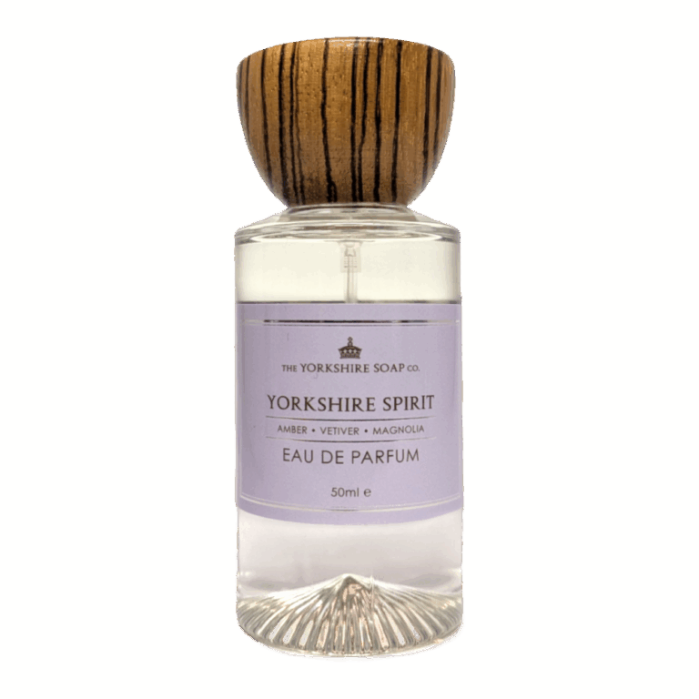 A tall cylindrical clear glass bottle full of some clear liquid with a circular dark wooden lid and a pale lavender label that has The Yorkshire Soap Company Yorkshire Spirit Eau De Parfum written in bold black writing and a picture of a black crown on it, on a white background.