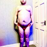 I Saw A Prophecy That This Might Be A Really Comfy Thong | Kiniki Orange Apollo Thong A tall bearded man with his arms resting by his sides wearing a bright orange thong with a bright orange waistband that has Kiniki written in bright white writing on it stood against a white wooden door.
