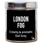 Tea Tastes Terrific | Bird & Blend Tea Company London Fog Loose Leaf Tea A tall cylindrical bright silver metal tin with a bright silver metal lid and a black label that has London Fog loose Leaf Tea written in bright white writing and a picture of two bright white leaves on it, on a white background.