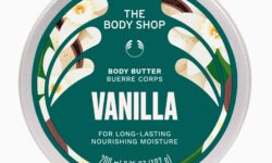 A short cylindrical Silver Metal Tin with a silver metal lid and a dark Green label that has The Body Shop Vanilla Body Butter written in bright white writing, some pictures of some small creamy white Vanilla Flowers, and some pictures of some dark Brown Vanilla Pods on it, on a white background.