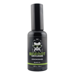 A tall cylindrical Black Glass Bottle with a matte Black Plastic lid and a black label that has Bigfoot Grooming written in bright green writing, Lemongrass Beard Oil written in bright white writing, a picture of a bearded man with some styled hair wearing a pair of green sunglasses, and a bright green stripe on it, on a white background.