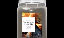 A tall cylindrical glass Jar full of some pale Grey Wax with a bright white label that has Yankee Candle written in bold black writing, Crackling Embers written in bold black writing, and a picture of some burning kindling and some bright red, orange and yellow glowing embers on it, on a black background.