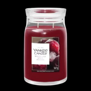 A tall cylindrical glass Jar full of some Dark Red Wax with a bright white label that has Yankee Candle written in bold black writing, Woodland Spice written in bold black writing, and a picture of some frosted dark red berries on it, on a black background.
