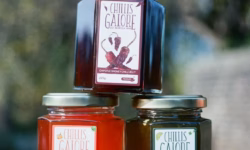 A short hexagonal clear glass jar full of some dark red chilli jam with a bright gold metallic lid and a bright white label that has Chillis Galore Chipotle Smokey Chilli Jam written in dark Red writing and some pictures of some dark red chilli Peppers on it next to a short hexagonal clear glass jar full of some bright red chilli jam with a bright gold metallic lid and a bright white label that has Chillis Galore Jamaican Peppers Chilli Jam written in bright red writing and some pictures of some dark orange scotch chilli peppers on it, and a short hexagonal clear glass jar full of some dark olive green chilli jam with a bright gold metallic lid and a bright white label that has Chillis Galore Jalapeno & Coriander Chilli Jam written in dark green writing and some pictures of some bright green chilli Peppers and some dark green coriander leaves on it, on a white background.