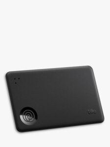 A medium rectangular black plastic credit card with some rounded corners that has a raised spiral logo, three circular speaker holes, and Tile engraved on it, on a white background.