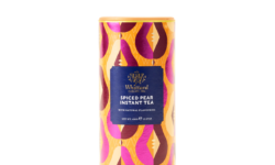 A tall cylindrical bright Brown, Magenta, Pink, Orange and Yellow abstract patterned cardboard tube with a bright yellow plastic lid and a bright blue label that has Whittard of Chelsea written in bright gold writing and Spiced Pear Instant Tea written in bright white writing on it, on a white background.